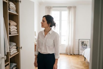 Femme devant un dressing organisé avec des vêtements basiques bien rangés, chemise blanche et pantalon marine